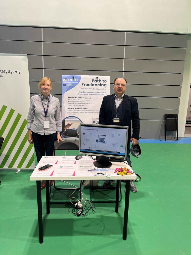 The project coordinator and the project manager at the ENTEEF stall - Path to Freelancing poster in the background, in front a table with examples of microcredencials, monitor dislaying ENTEEF video, leafleats, and sweets.